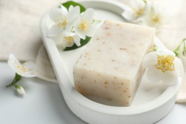 Sabun çubuğu ve yasemin çiçekleri beyaz masada, yakın plan.