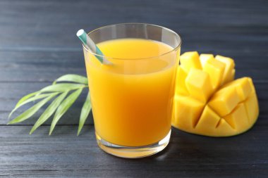 Bardakta lezzetli mango suyu, taze meyve ve ahşap masada yeşil yapraklar, yakın plan.