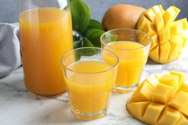 Bardakta lezzetli mango suyu, taze meyve ve yeşil yapraklar beyaz mermer masada, yakın plan.