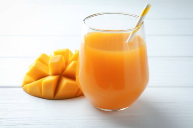 Bardakta lezzetli mango suyu ve beyaz ahşap masada taze meyve, yakın plan.