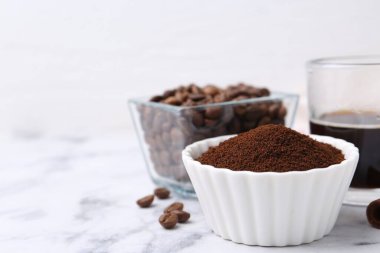 Kâsede kahve tozu, fasulye ve içecek beyaz mermer masada, yakın plan. Metin için boşluk