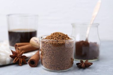 Granüle edilmiş hazır kahve ölçü kabı ve baharatlar gri masada, yakın plan.