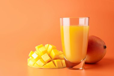 Bardakta lezzetli mango suyu ve turuncu arka planda taze meyve.