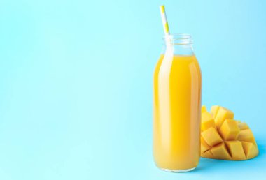 Cam şişede lezzetli mango suyu ve açık mavi arka planda taze meyve, mesaj için yer var.