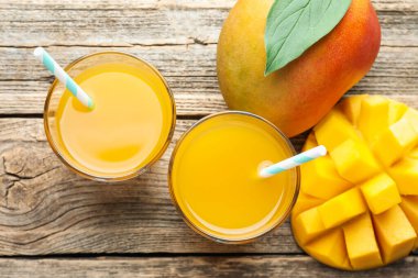 Bardakta lezzetli mango suyu ve ahşap masada taze meyveler.