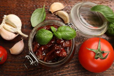 Lezzetli güneş, cam kavanozda kurutulmuş domatesler, ahşap masada taze sebzeler ve baharatlar, düz uzanmış.