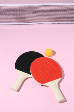 Masa tenisi raketleri, top ve net pembe arka planda, görünümün üstünde.