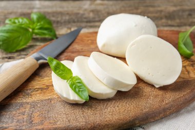 Ahşap masada fesleğen ve bıçakla mozzarella peyniri kes, yakın plan.