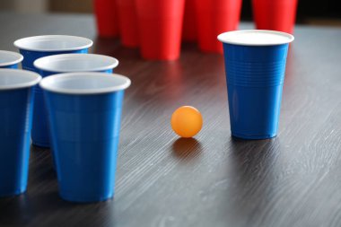 Bira pong oyunu. İçkili plastik bardaklar ve tahta masada top, yakın plan.