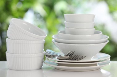 Beyaz masadaki farklı temiz tabaklar, bulanık yeşil arka plan, yakın plan