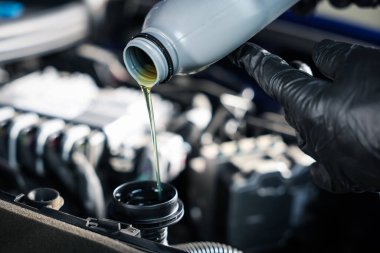 İşçi şişeden araba motoruna motor yağı döküyor.