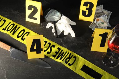 Adli tıp uzmanı. Sarı olay yeri bandı, siyah masanın üstünde işaretler ve kanıtlar var.