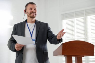 İçerideki kürsüde mikrofonla halka açık konuşma yapan adam.