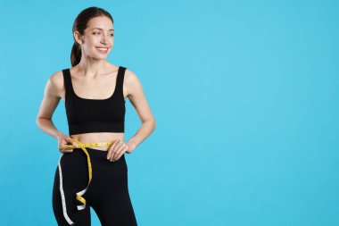 Güzel bir kadın göbeğini açık mavi arka planda bantla ölçüyor.