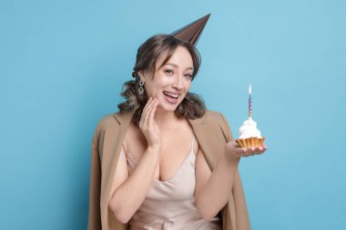 Doğum günü kutlaması. Açık mavi arka planda kek yiyen kadın.