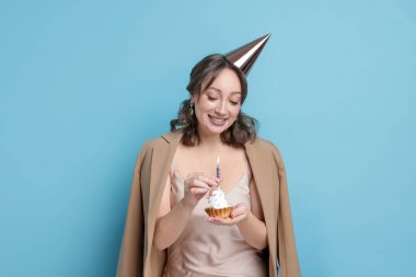 Doğum günü kutlaması. Açık mavi arka planda kek yiyen kadın.