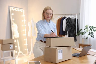 Dükkan sahibi, terzi dükkanında paketlerle birlikte masada notlar alıyor.