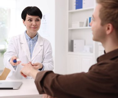 Oftalmolog, klinikteki beyaz masadaki hastaya kontak lensleri veriyor.