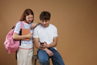 Sırt çantası, kitapları ve kahverengi arka planda akıllı telefonu olan gençler. Metin için boşluk