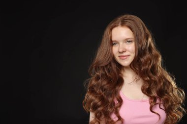 Siyah arka planda sağlıklı dalgalı saçları olan güzel bir genç kız. Metin için boşluk