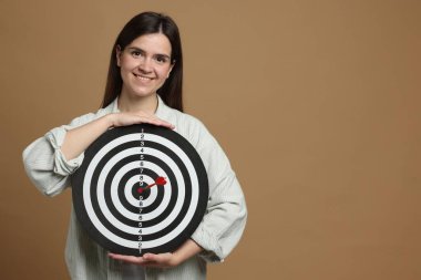 Hedef alınıyor. Bej arka planda ok ve dart tahtası olan gülümseyen kadın. Metin için boşluk
