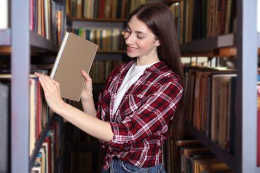 Halk kütüphanesindeki raftan kitap alan kadın.