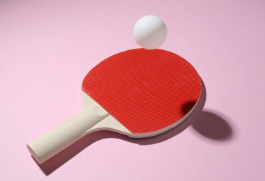 Pembe arka planda pinpon raketi ve top, yakın plan.
