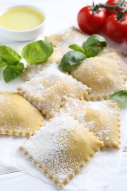 Pişmemiş ravioli, fesleğen, domates ve yağ beyaz ahşap masada, yakın plan.