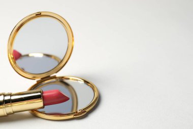 Açık cep aynası ve açık gri arka planda ruj, yakın plan. Metin için boşluk