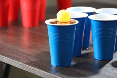 Bira pong oyunu. İçkili plastik bardaklar ve tahta masanın üzerinde top, yakın plan. Metin için boşluk