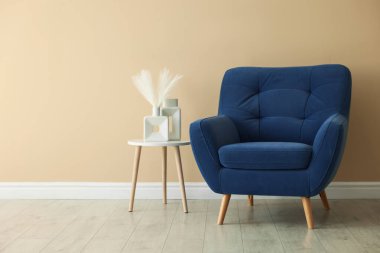 Rahat mavi koltuk ve masa. Bej duvarın yanında vazolar, metin için yer var.