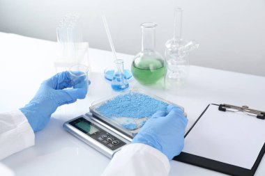 Bilim adamı beyaz ayna masasındaki terazide numune tartıyor, yakın plan.