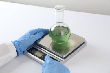 Bilim adamı beyaz masadaki terazide numune tartıyor, yakın plan.