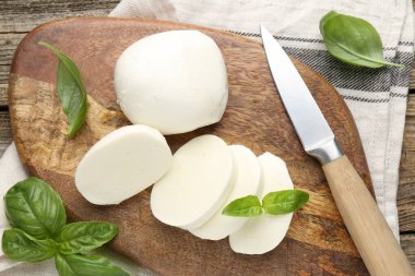 Ahşap masada fesleğen ve bıçakla mozarella peyniri kes.