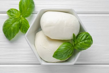 Lezzetli mozzarella peyniri ve fesleğen parçaları beyaz ahşap masada, düz yatıyordu.