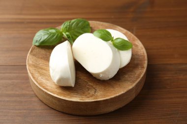 Nefis mozzarella peyniri parçaları ve fesleğen yaprakları ahşap masada, yakın plan.