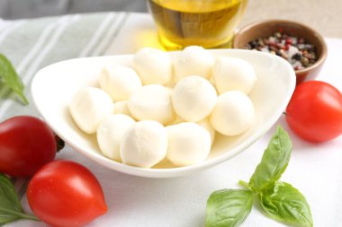 Lezzetli mozzarella peynir topları, domates, fesleğen, yağ ve biberler masada, yakın plan.