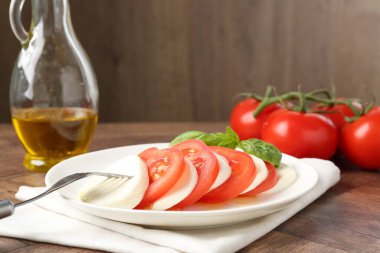 Lezzetli mozzarella, domates, yağ ve fesleğen ahşap masada, yakın plan.