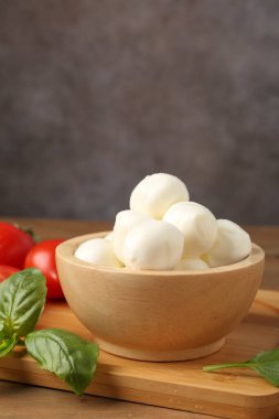 Lezzetli mozarella topları, domatesler ve fesleğenler ahşap masada, yakın plan.