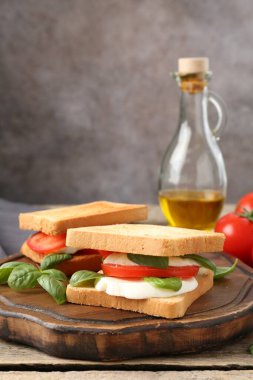 Mozarella peynirli, domatesli ve ahşap masadaki fesleğenli lezzetli sandviçler.