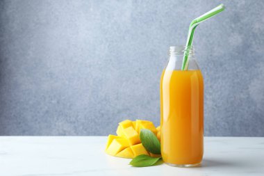Cam şişedeki lezzetli mango suyu, taze meyve ve yeşil yapraklar beyaz mermer masada, mesaj için yer var.