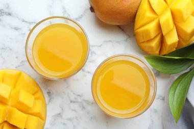 Lezzetli mango suyu bardakta, taze meyve ve yeşil yapraklar beyaz mermer masada, düz yerde