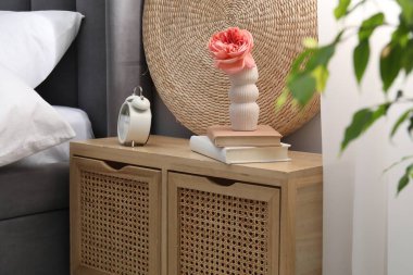 Yatağın yanında çalar saati, dekorasyonu ve kitapları olan bir komodin.