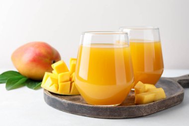 Bardakta lezzetli mango suyu, taze meyve ve yeşil yapraklar beyaz masada, yakın plan.