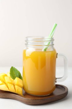 Cam mason kavanozunda lezzetli mango suyu, beyaz masada taze meyve ve nane, yakın plan.