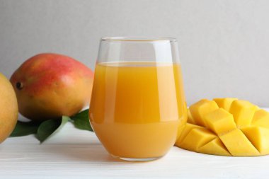 Lezzetli mango suyu bardakta, taze meyve ve yeşil yapraklar beyaz ahşap masada, yakın plan