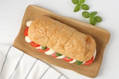 Mozarella peynirli, domatesli, fesleğenli, beyaz ahşap masadaki lezzetli sandviç.