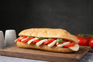 Mozarella peynirli, domatesli ve fesleğenli lezzetli sandviç. Gri desenli masa, koyu arkaplanlı, yakın plan.