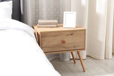 Yatağın yanında kitap ve çerçeve olan komodin.