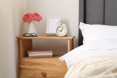 Alarm saati, çiçekler ve yatağın yanındaki dekorlu komodinin yanında.
